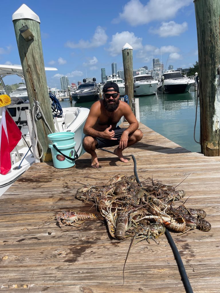 A person squatting next to a pile of lobsters caught in North Miami