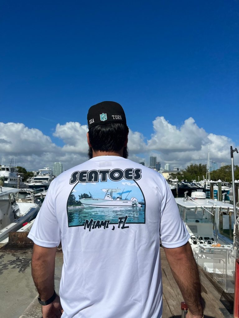 A person wearing a white shirt with a boat picture from Sea Toes Charters