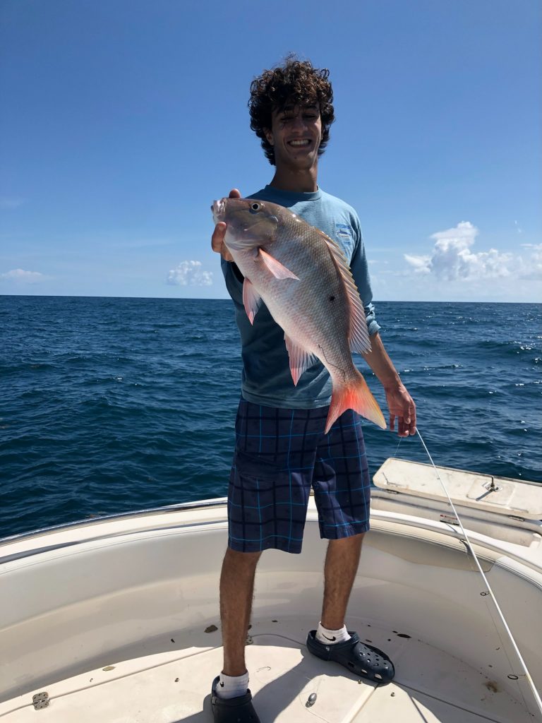 An angler holding a fish on a boat during a Brickell trip