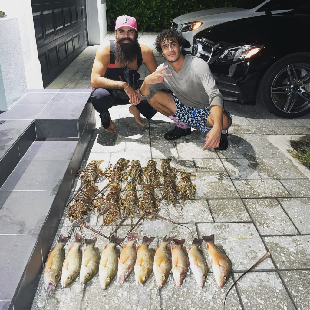 Two men kneeling next to a row of fish caught in North Miami