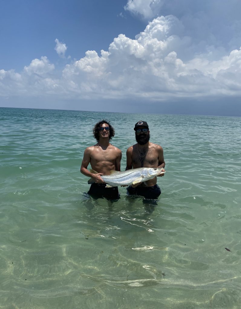Two men displaying a fish in the water near North Miami