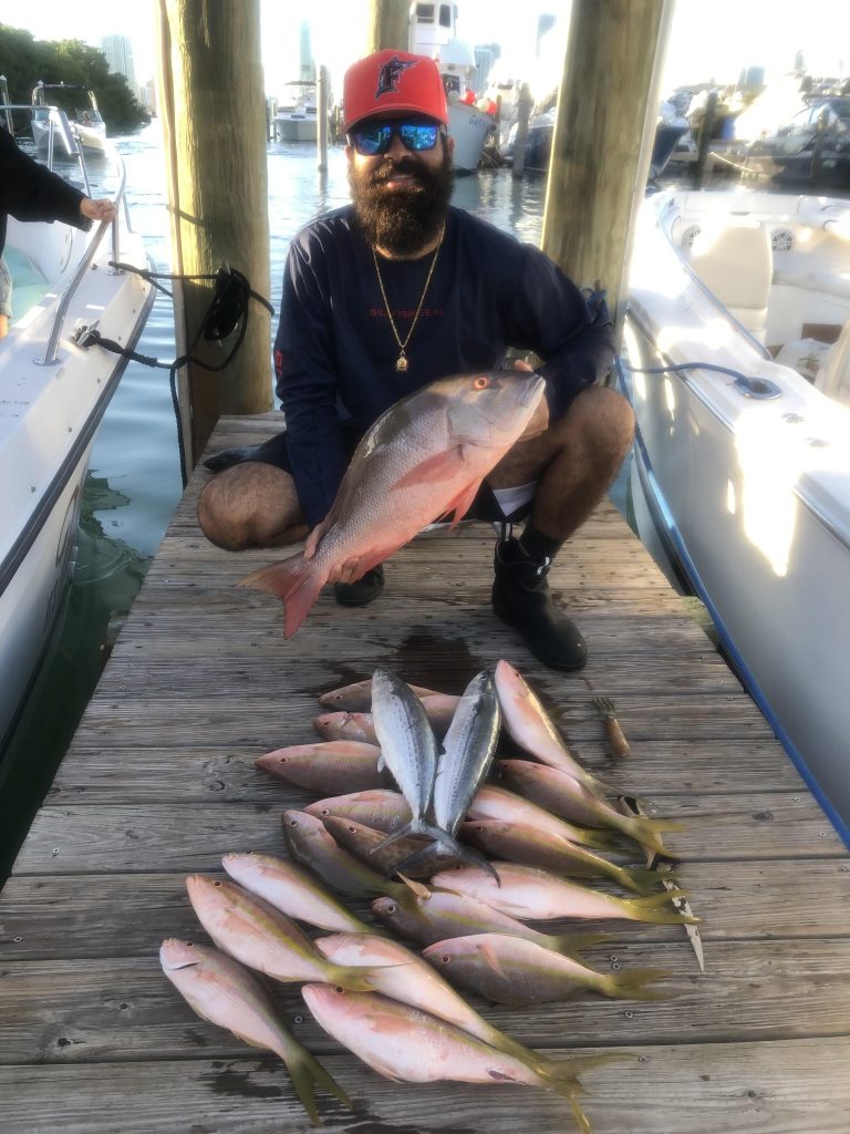 An angler sitting on a dock with a fish and a pile of fish